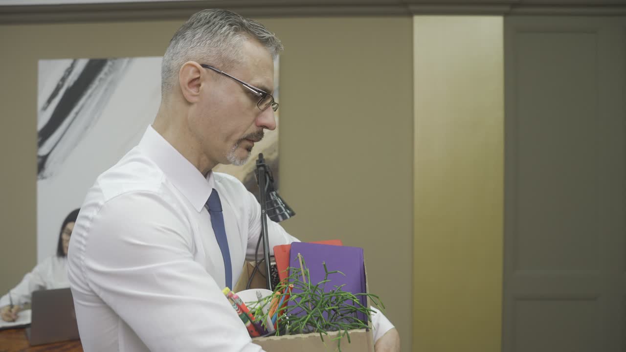 흰색 셔츠와 회색 넥타이를 매고 개인 물건을 상자에 넣고 사무실을 떠나는 우아한 남자