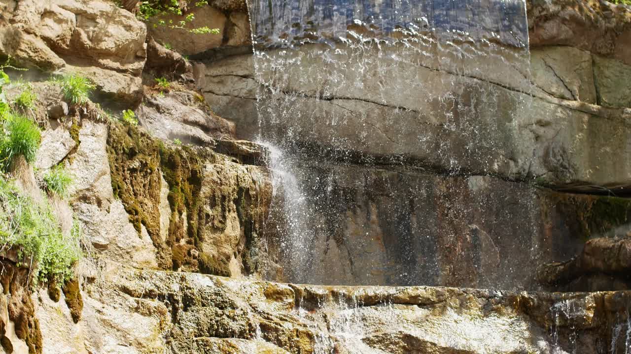 Beautiful waterfall from a cliff in the forest. 4K video of flowing water, flowing stream among stones. Stream in the forest