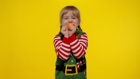 niña con disfraz de ayudante de santa claus atrapando frutas de mandarina. celebración de vacaciones de año nuevo