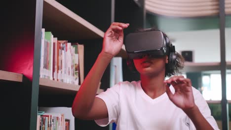 a schoolgirl sitting in front of library's bookshelf and using virtual reality glasses.
