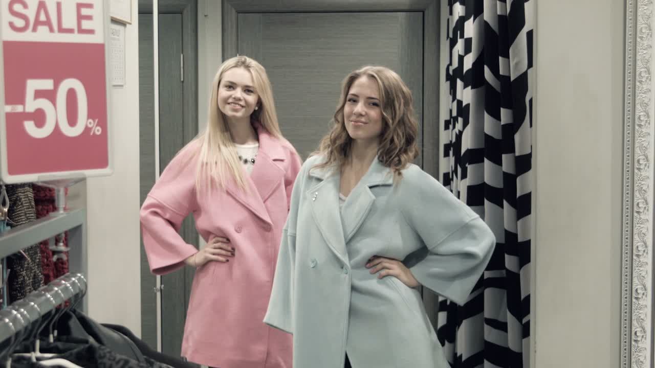 Two Girls Try On a Coat In a Locker Room