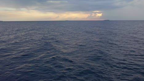 Aerial,-drone-shot,-low-close-to-the-surface,-over-a-dark-phantom-blue-sea,-on-the-Indian-ocean,-on-a-partly-sunny-evening,-in-the-Maldives-islands