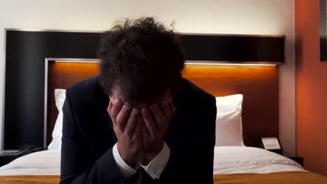 male in business clothing sitting frustrated on hotel room bed