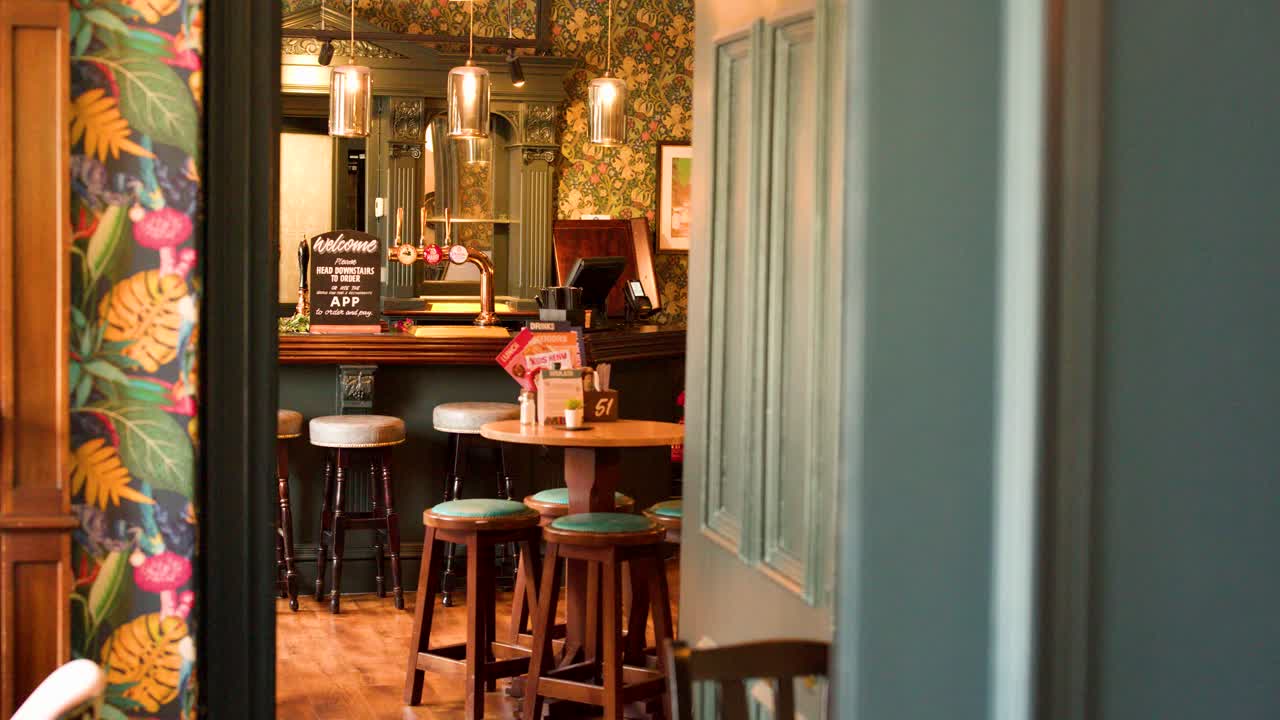 Camera glides through doorway, revealing warmly lit vintage pub with floral wallpaper and bar stools