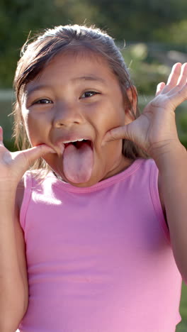 vertical video: girl in pink shirt making funny face and sticking out tongue outdoors