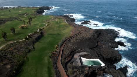 Drone-Shot-Towards-Blue-Ocean-with-White-Waves-By-Green-Golf-Resort