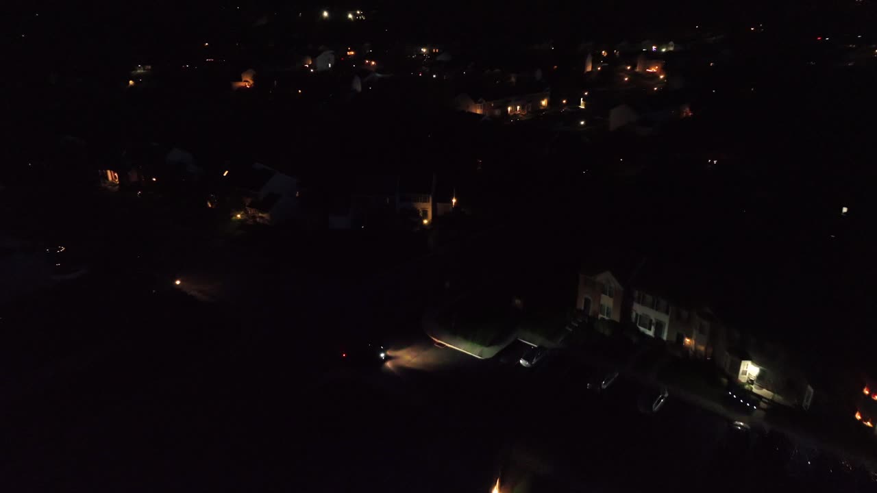 Car with headlights in American neighborhood at night. Arriving home at midnight. Aerial approaching shot. Luxury housing area in United States.