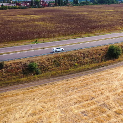 flying over field near the highway. white audi moving slowly on the road on the background of rural landscape. aerial view.