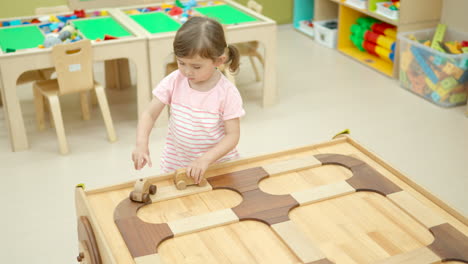 girl toddler plays with wooden toy cars pushing them along the road on wood table in playroom - slow motion