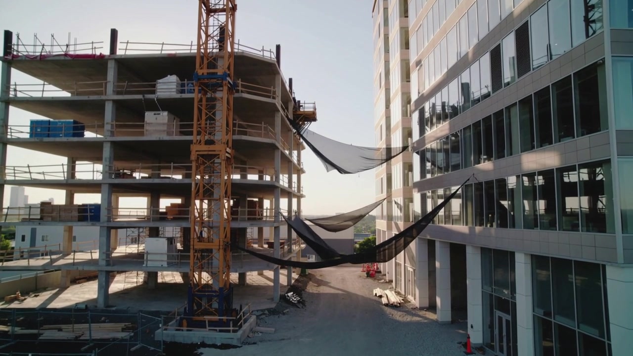 Moving camera showing site between buildings, tower crane and three black nets settling in breeze