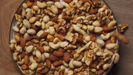 close up overhead shot of nuts falling into bowl containing cashews dry roasted peanuts pistachio walnuts and hazelnuts 1