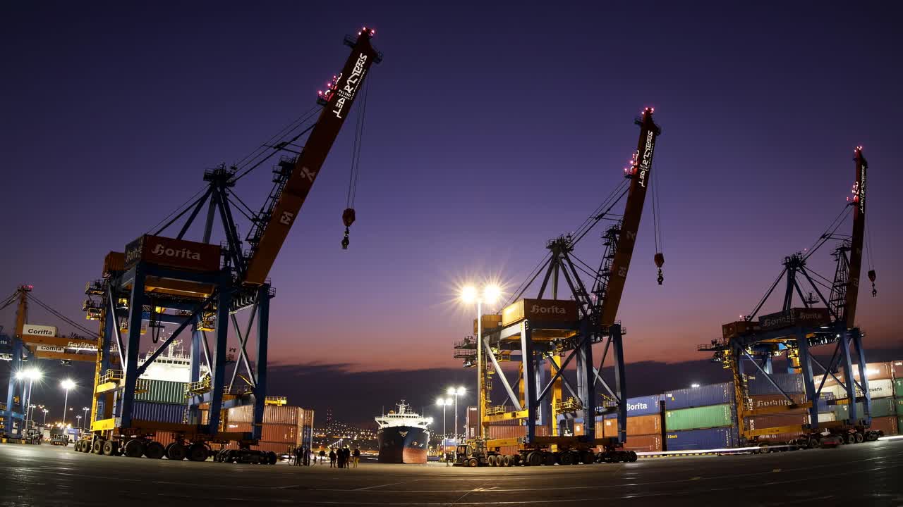 Wide-angle shot of a bustling port at dusk, featuring towering cranes and containers