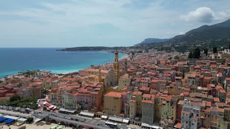 Casco-Histórico-De-La-Ciudad-Costera-De-Menton,-Francia,-Con-La-Iglesia-Basílica-De-San-Miguel-Y-La-Carretera-Principal-Del-Océano,-Toma-Aérea-A-La-Derecha