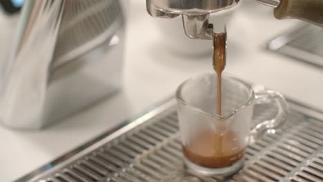 Amber-brown-coffee-drips-into-glass-cup-on-metal-grate-in-white-cafe