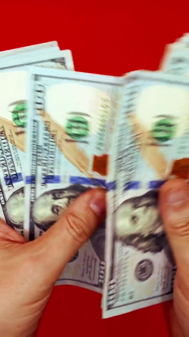 B-roll verticale 9:16: mani che sventagliano banconote da 100 dollari su sfondo rosso. Concetto per denaro veloce, motivazione alla ricchezza, transazione illegale, pagamento di stipendio, affari sul dark web e successo finanziario.