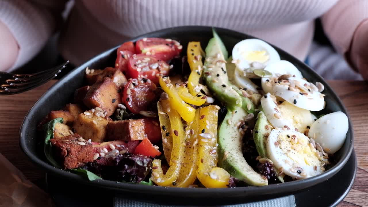 Close up of a woman eating a salad in a black bowl at a restaurant