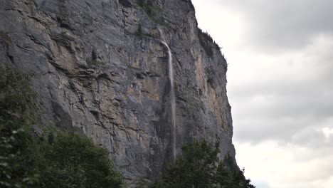 water falling down between the rocks and green pine trees from a high waterfall in lauterbrunnen in switserland on a cloudy day. wide shot
