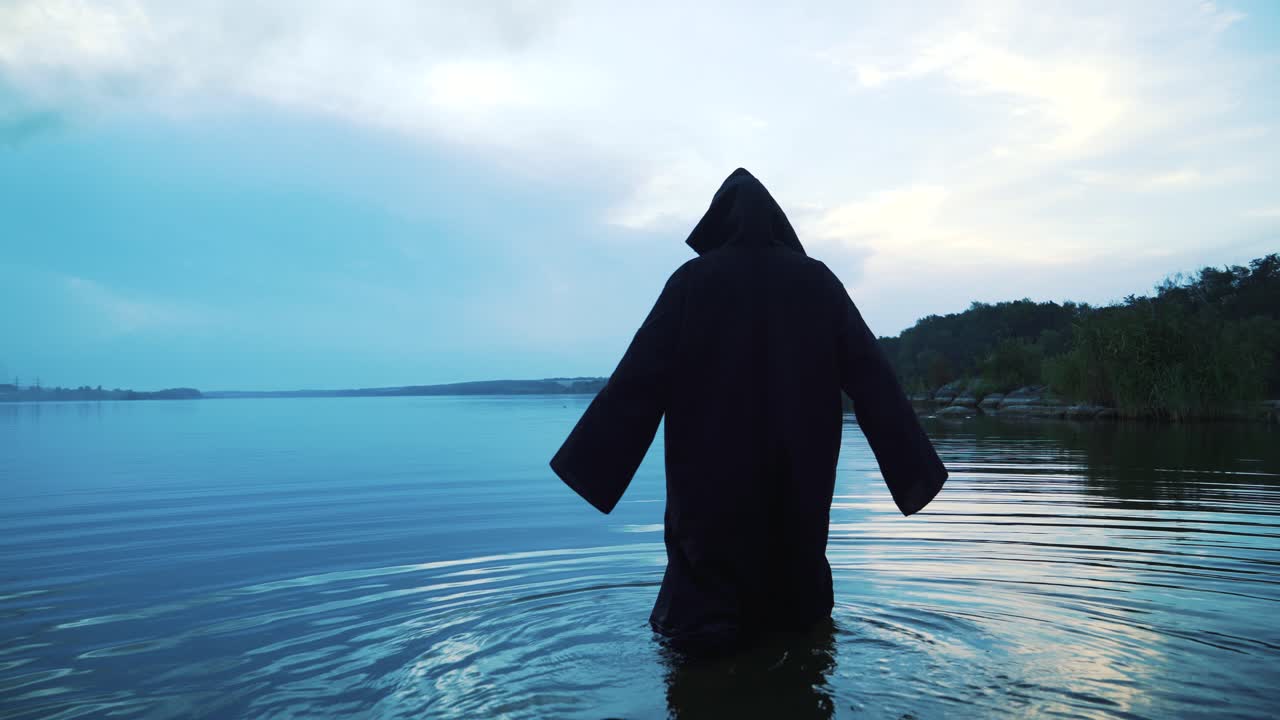 Scary figure in black mantle in the river. Halloween costume.