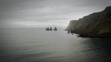 cinematic rock formation and cliff aerial black sand beach ocean scenery, moody dark scenery, town vik, reynisdrangar iceland