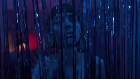 a young woman's face appears through glittering curtain