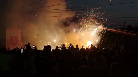 a large group of people filming fireworks and a fire show on their mobile phones. vibrant flames and colorful fireworks light up the night sky, creating an electrifying atmosphere