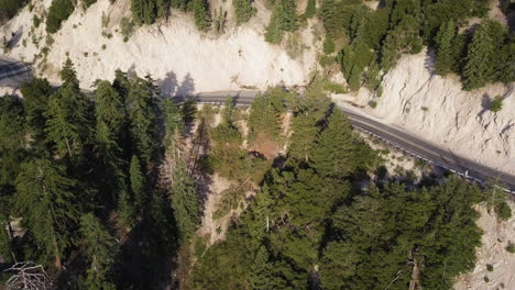 Vehículo-Suv-Oscuro-Conduce-Rápidamente-Por-Una-Carretera-De-Dos-Carriles-A-Través-De-Una-Montaña-Seca-Y-Un-Paisaje-De-Pinos