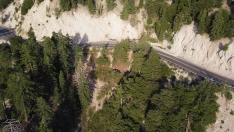 vehículo suv oscuro conduce rápidamente por una carretera de dos carriles a través de una montaña seca y un paisaje de pinos