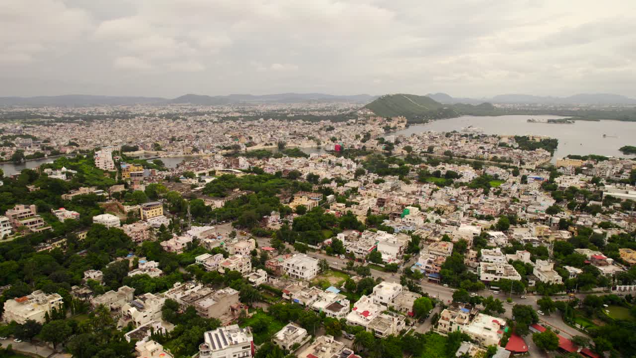 Volo aereo sopra case ed edifici a Udaipur con il lago Fateh Sagar sullo sfondo.