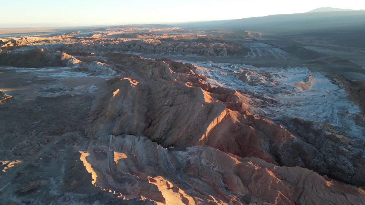 Cinematic drone footage flying over the barren landscape of Valle de la Luna, with dramatic cliffs and pastel skies at dusk.