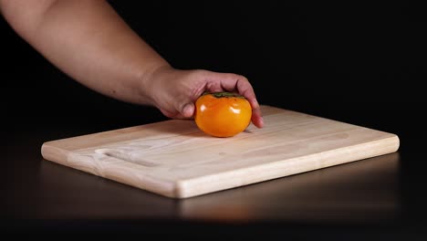 hand places persimmon on wooden cutting board