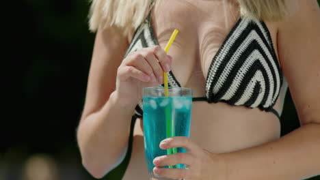 attractive woman in bikini shatters ice in a cocktail, close-up shot.