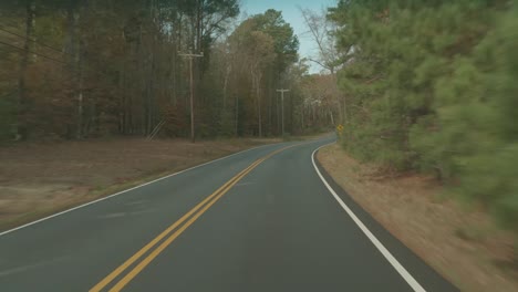 Driving-down-a-two-lane-country-road-at-fall-time,-winding-through-the-countryside