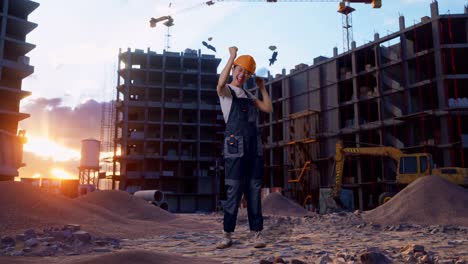 cuerpo lleno de trabajadora asiática que usa gafas de protección y casco de seguridad bailando mientras está de pie en el sitio de construcción