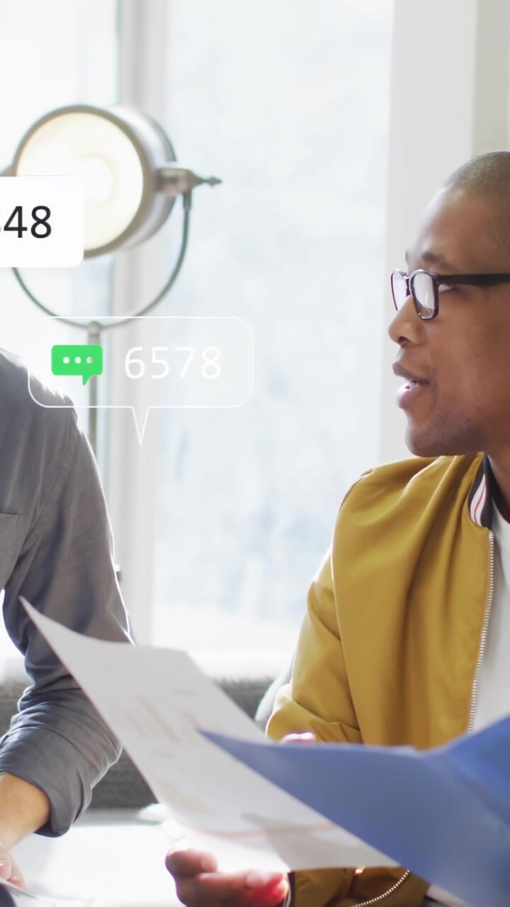 Vertical video: Reading jacketed man on sofa as metrics rise, woman taking blue folder smiling