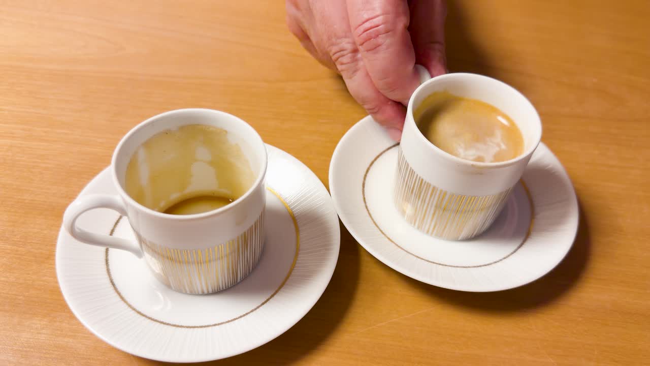 Una mano prende una tazzina da caffè in porcellana bianca da un piattino su un tavolo di legno.