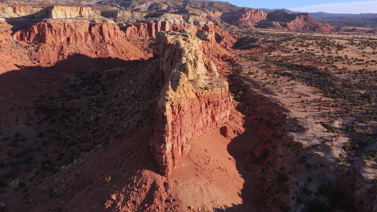 Una drammatica prospettiva da drone cattura le creste di arenaria stratificate di Abiquiu, Nuovo Messico. Questo aspro paesaggio desertico presenta affilate formazioni rocciose verticali contro un vasto altopiano baciato dal sole