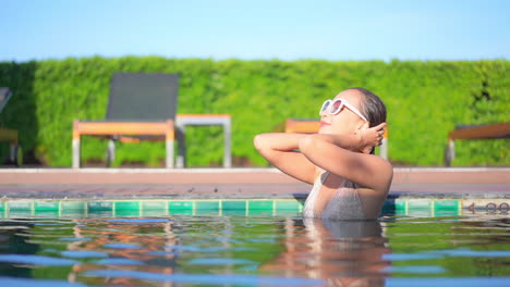 attractive exotic female caresses her wet hair in swimming pool on sunny summer day, full frame