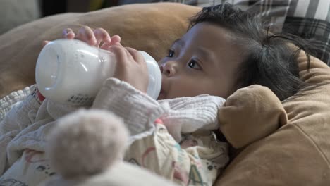 asian baby girl feeding on cows milk in bottle while lying down