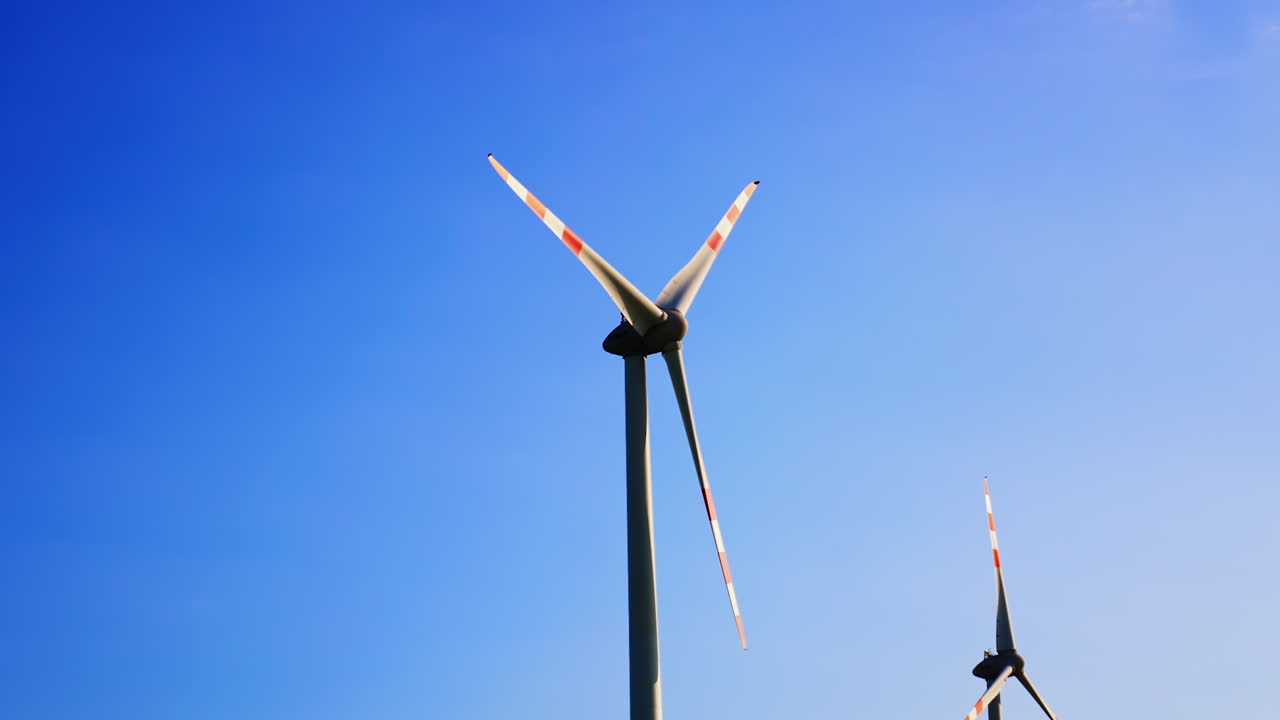 Wind turbines under a clear blue sky. Two wind turbines stand tall against a clear blue sky, showcasing renewable energy technology in action