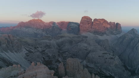 aerial view flying above jagged tre come south tyrol mountain range valley terrain with sunlit orange sunrise peaks