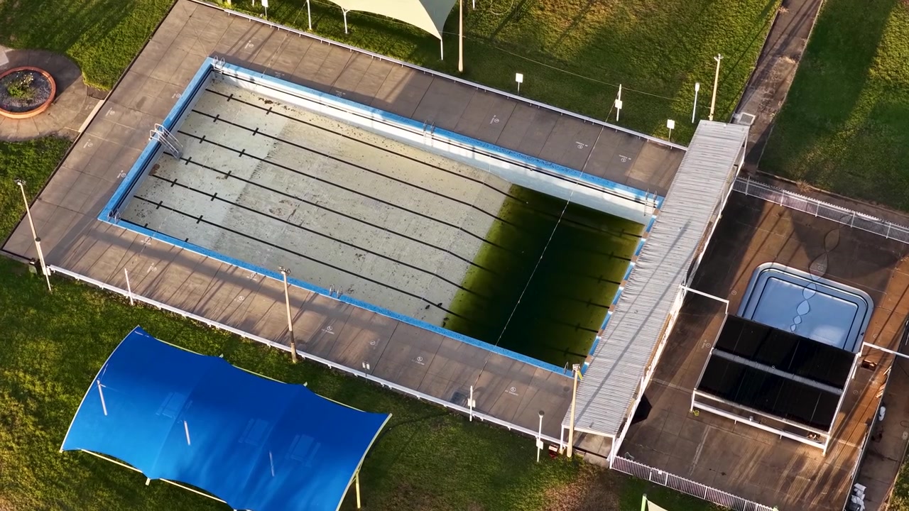 Vue aérienne par drone en plongée d'une piscine extérieure négligée avec des algues vertes en Australie