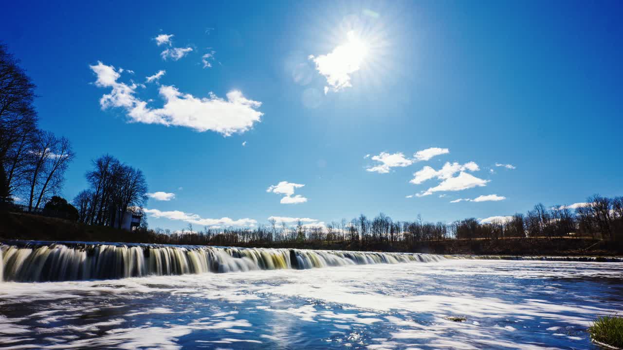 Wide time-lapse slow zoom reveals bright foamy river cascading in spring sun