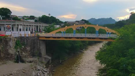 bright yellow and blue bridge croses over flowing green river, enters busy city