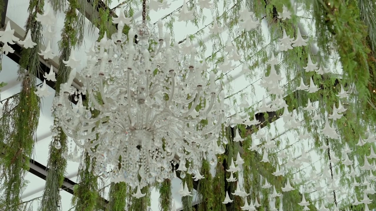 Elegant crystal chandelier illuminating an indoor ceiling decorated with beautiful white bell flowers and lush green foliage for a special event