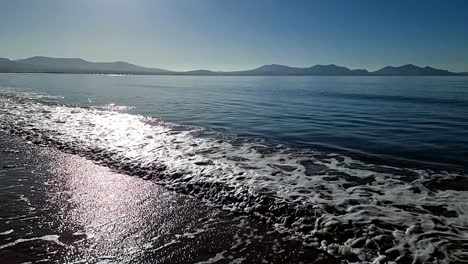 Cámara-Lenta,-Relajantes-Olas-De-Marea-Chapoteando-Bajo-El-Celestial-Y-Brumoso-Amanecer-De-La-Cordillera-De-Snowdonia