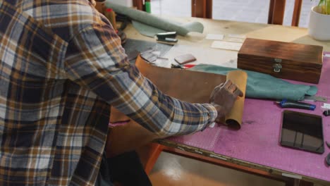 Midsection-of-african-american-craftsman-unrolling-leather-in-leather-workshop