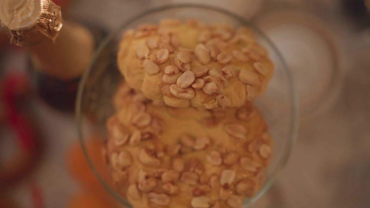 Biscotti alle arachidi impilati in una ciotola di vetro, luce calda e dorata, scatto ravvicinato dall'alto di due biscotti guarniti con noci appoggiati in un bicchiere da cocktail accanto a una bottiglia di champagne sfocata, dettagli della texture e briciole su un ambiente accogliente.