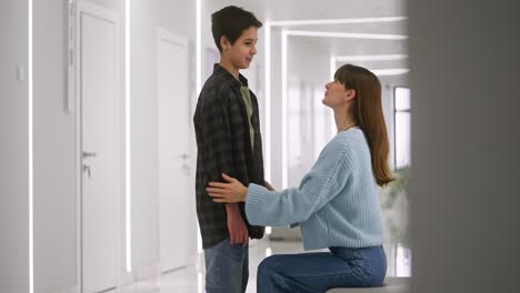 mother helping son with his shirt in a modern hospital corridor