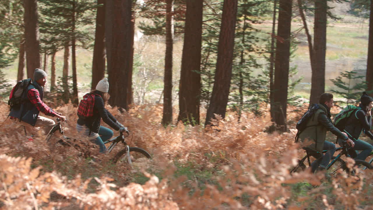 Friends riding bikes in forest, side view, left to right pan