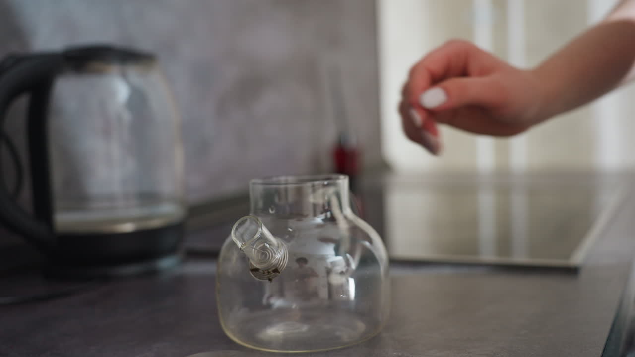 Caucasian Woman Placing Glass Jar Stove Careful Hands Set Sealed Jar On Induction Panel Near Kettle, Organizing Spices And Herbs, Quiet Kitchen Ritual Of Storage And Order, Domestic Neatness And Calm